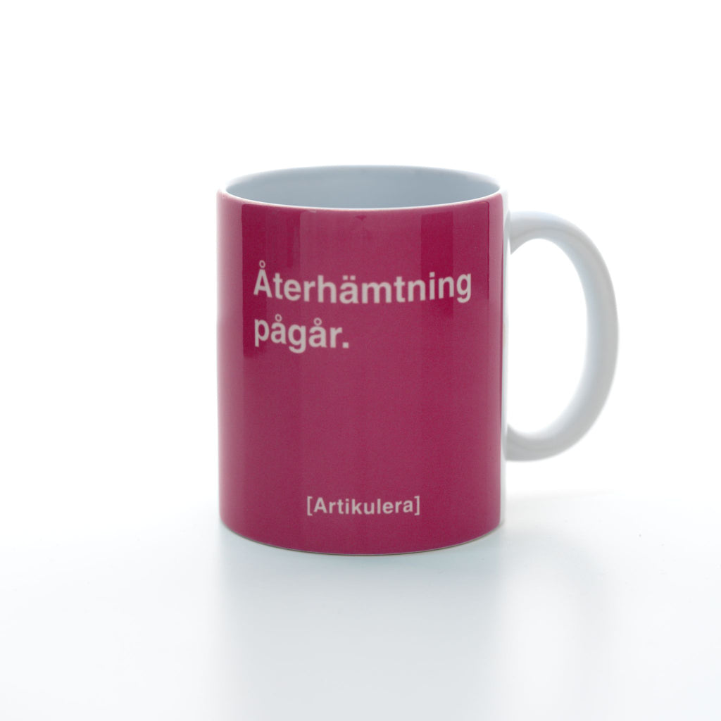 Vit mugg med cerise tryck, vit text ”Återhämtning pågår.” samt vit Artikulera-logotyp
