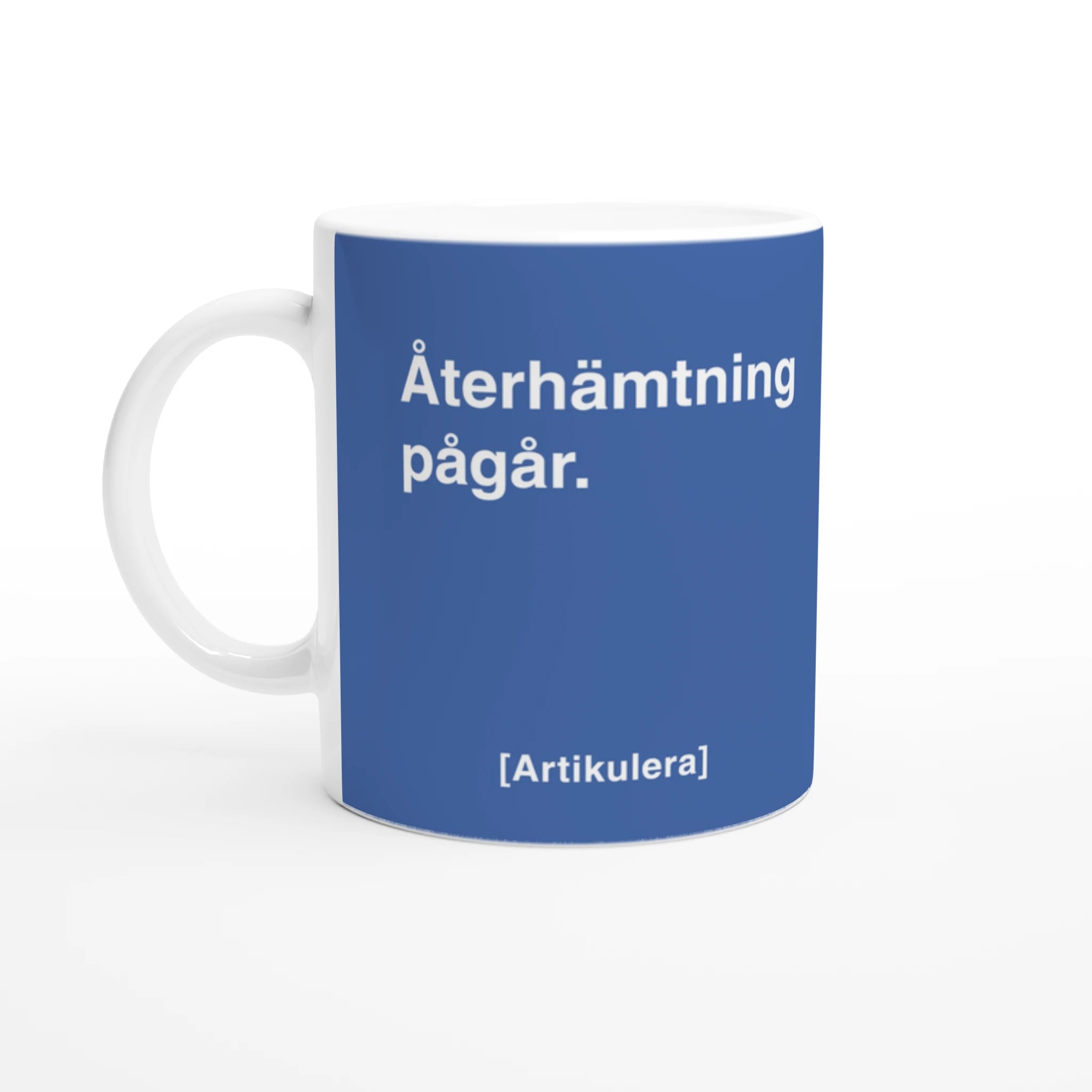 Vit mugg med duvblått tryck, vit text ”Återhämtning pågår.” samt vit Artikulera-logotyp