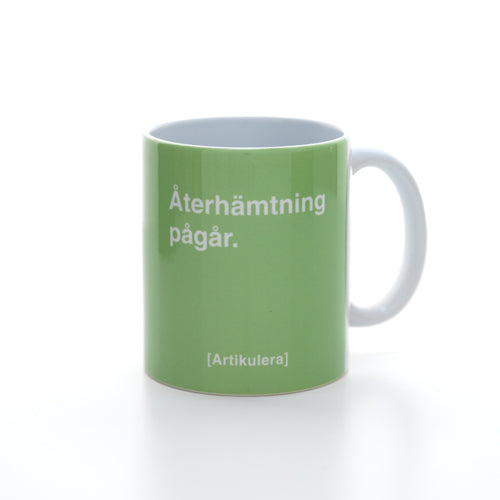 Vit mugg med ljus limegrönt tryck, vit text ”Återhämtning pågår.” samt vit Artikulera-logotyp