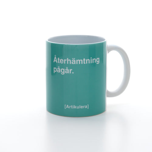 Vit mugg med mintrönt tryck, vit text ”Återhämtning pågår.” samt vit Artikulera-logotyp