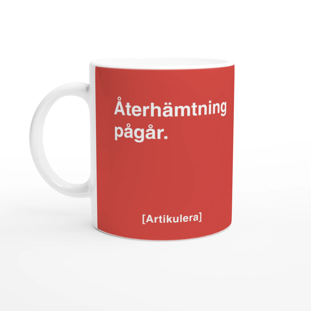 Vit mugg med tomatrött tryck, vit text ”Återhämtning pågår.” samt vit Artikulera-logotyp