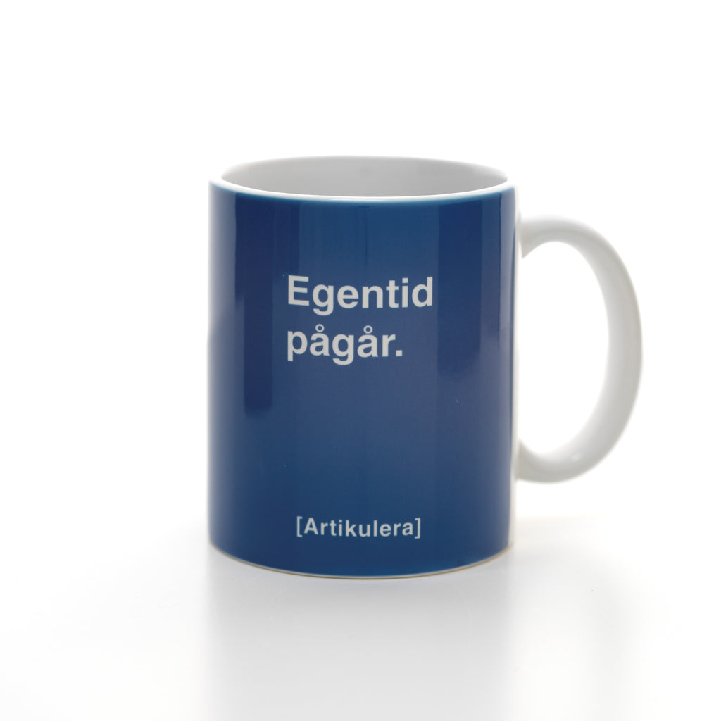Vit mugg med duvblått tryck, vit text ”Egentid pågår.” samt vit Artikulera-logotyp