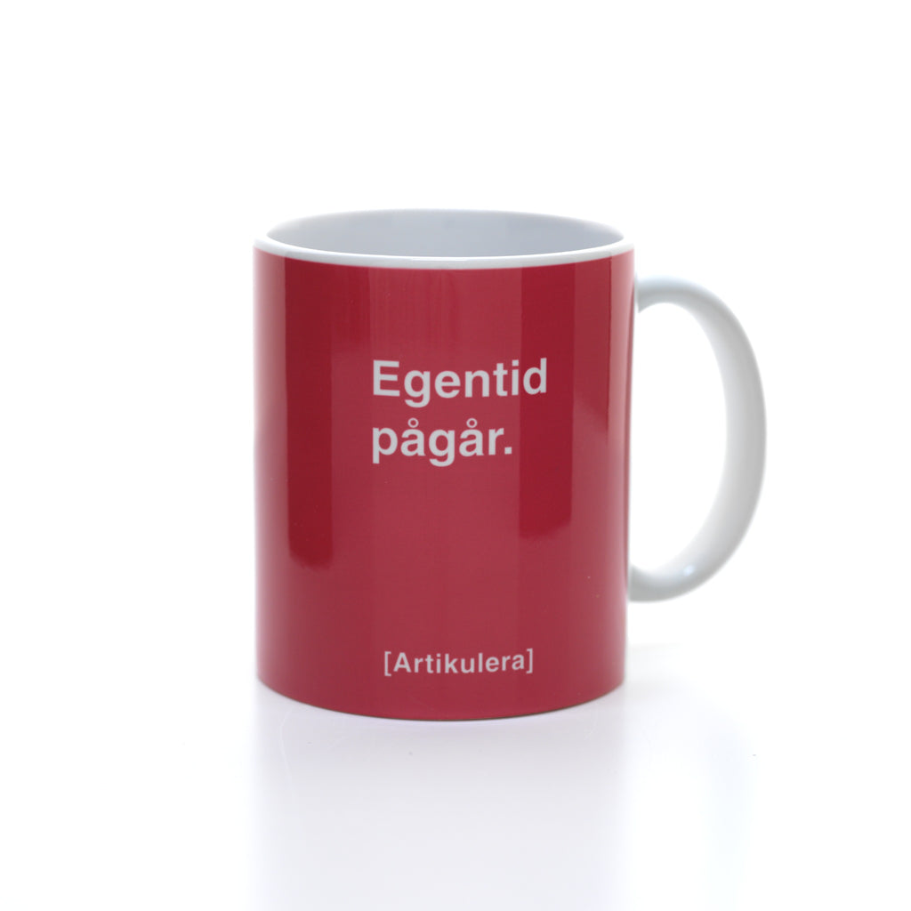 Vit mugg med magentarött tryck, vit text ”Egentid pågår.” samt vit Artikulera-logotyp