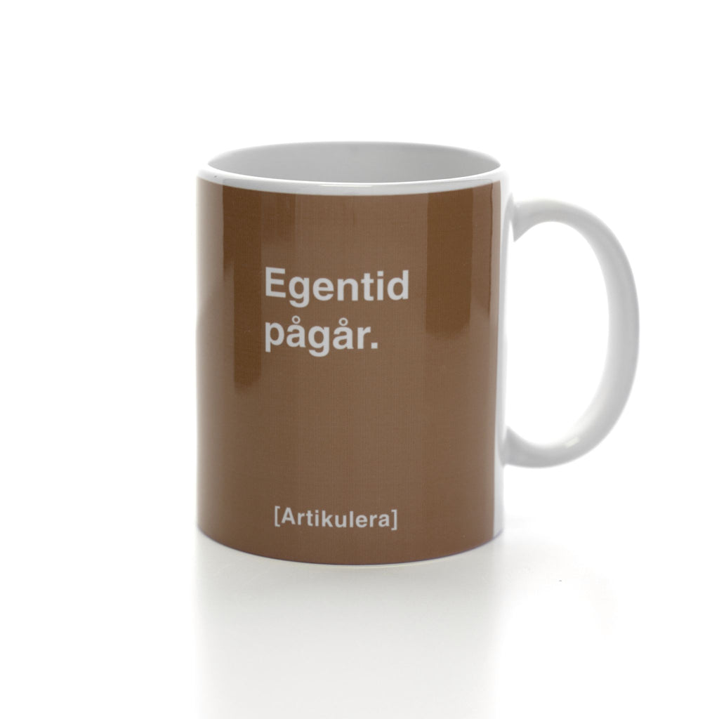 Vit mugg med mediumbrunt tryck, vit text ”Egentid pågår.” samt vit Artikulera-logotyp