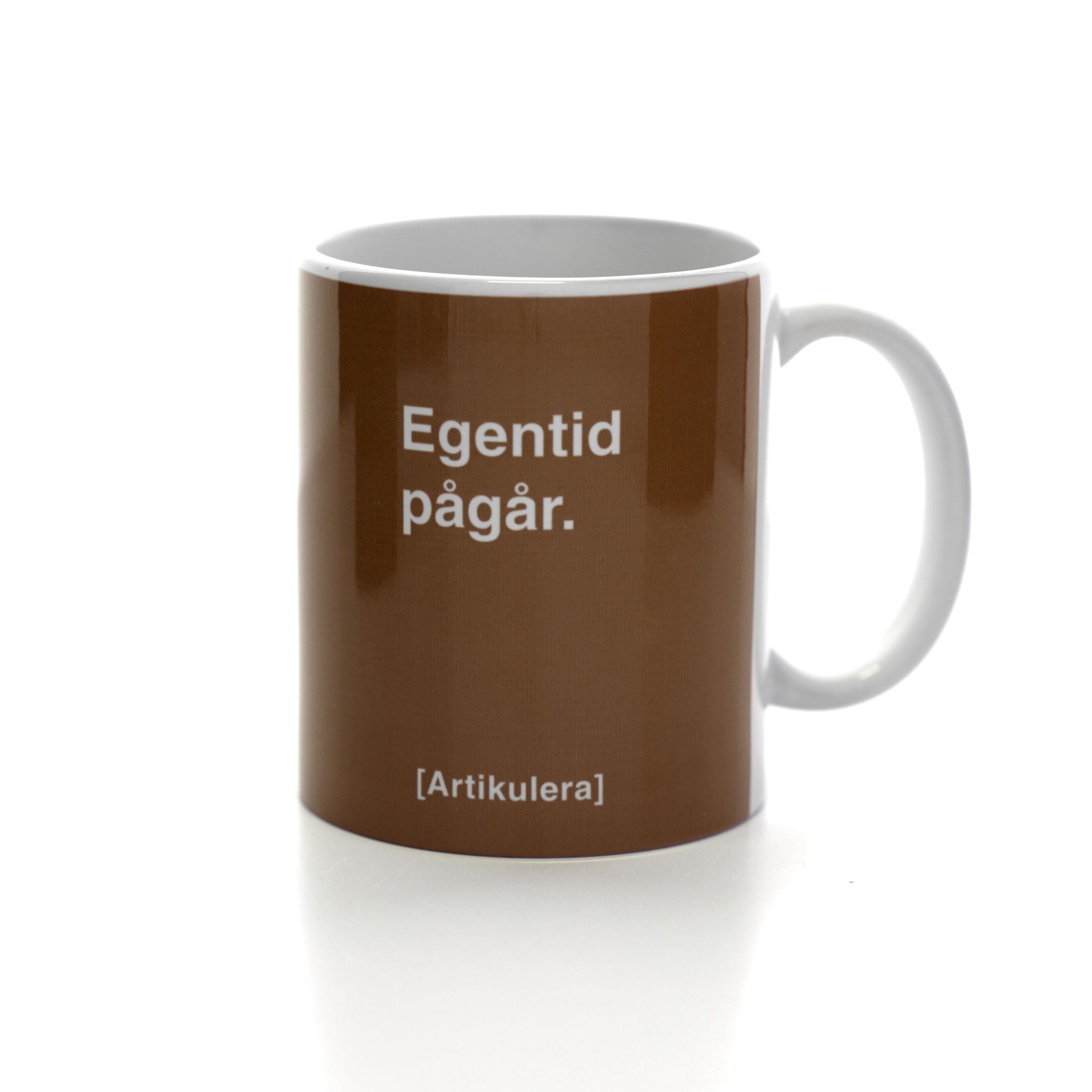 Vit mugg med mörkbrunt tryck, vit text ”Egentid pågår.” samt vit Artikulera-logotyp