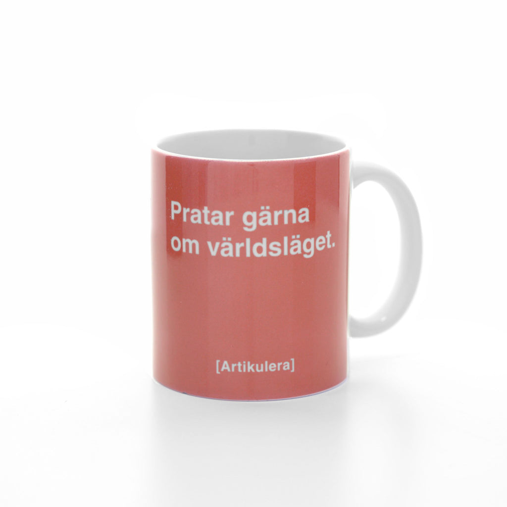 Vit mugg med korallrött tryck, vit text ”Pratar gärna om världsläget.” samt vit Artikulera-logotyp