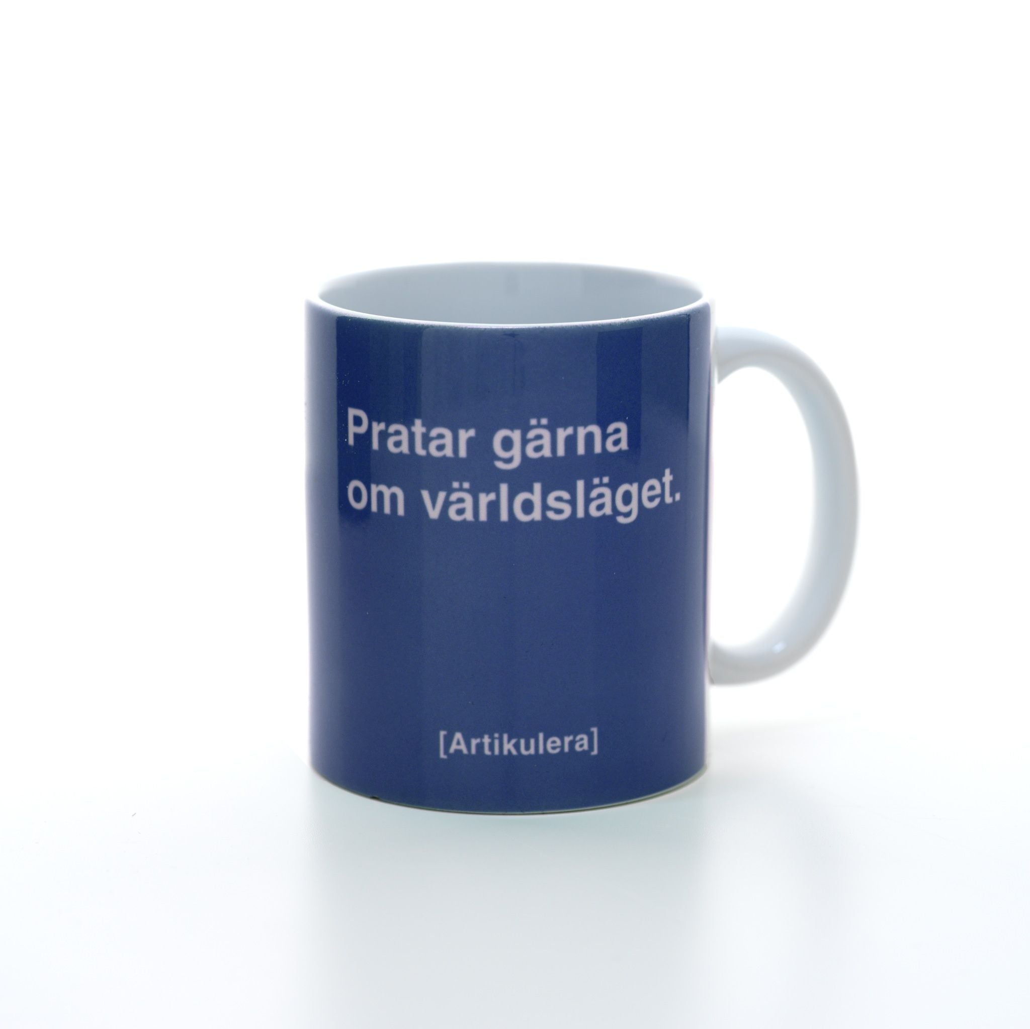 Vit mugg med duvblå tryck, vit text ”Pratar gärna om världsläget.” samt vit Artikulera-logotyp