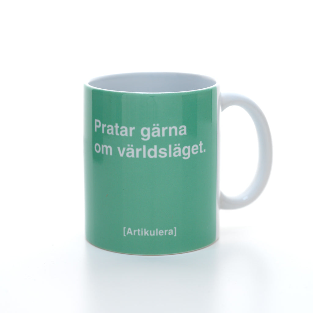 Vit mugg med grönt tryck, vit text ”Pratar gärna om världsläget.” samt vit Artikulera-logotyp