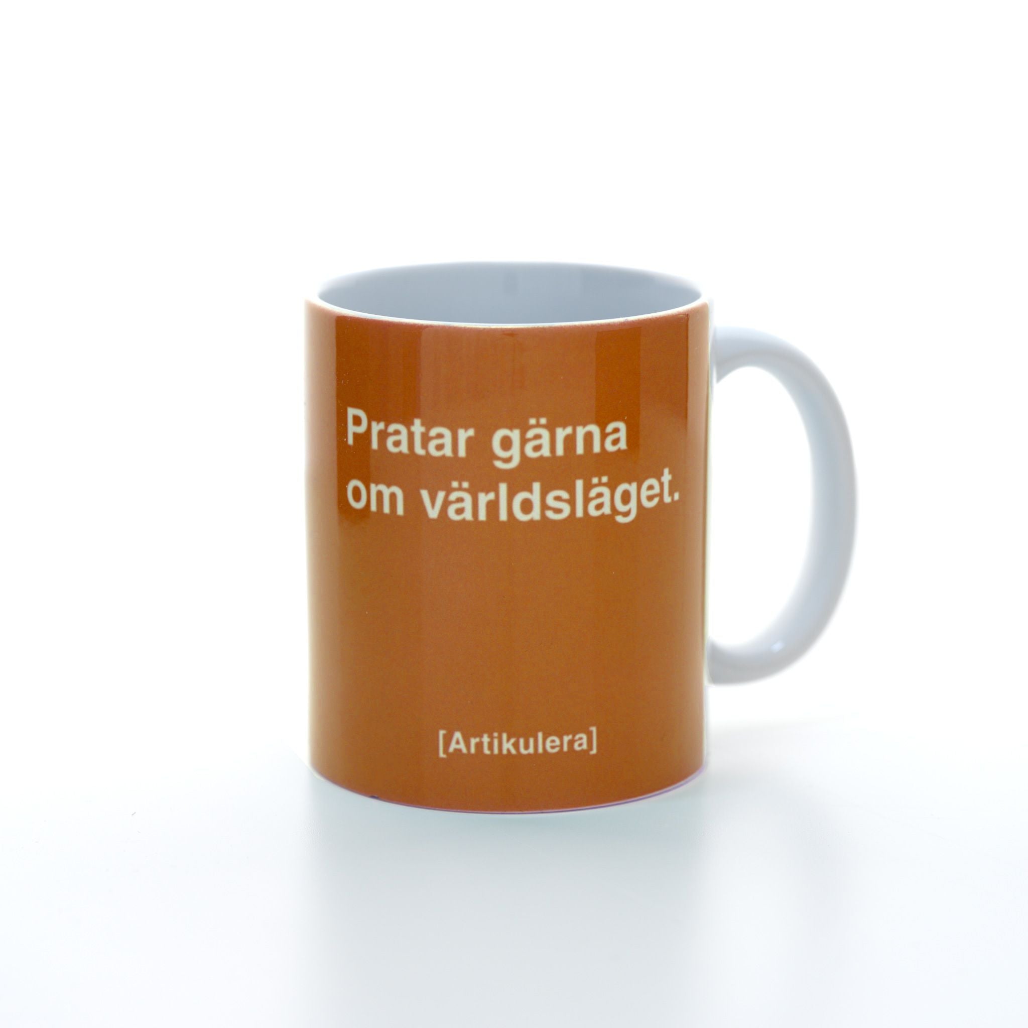 Vit mugg med mörkt orange tryck, vit text ”Pratar gärna om världsläget.” samt vit Artikulera-logotyp