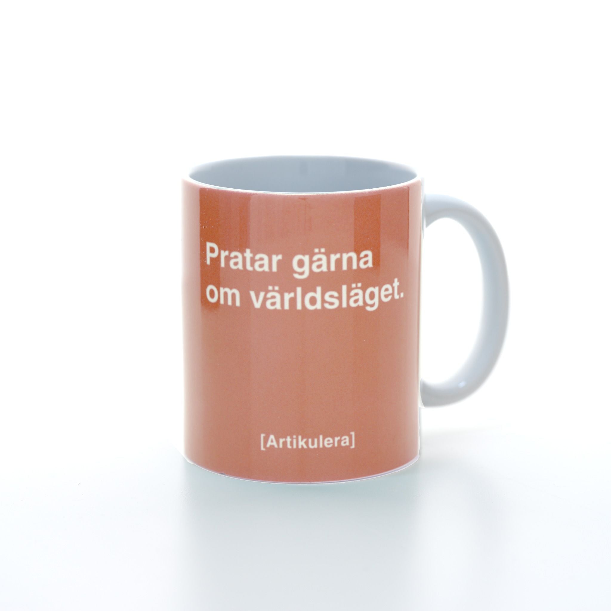 Vit mugg med persikofärgat tryck, vit text ”Pratar gärna om världsläget.” samt vit Artikulera-logotyp