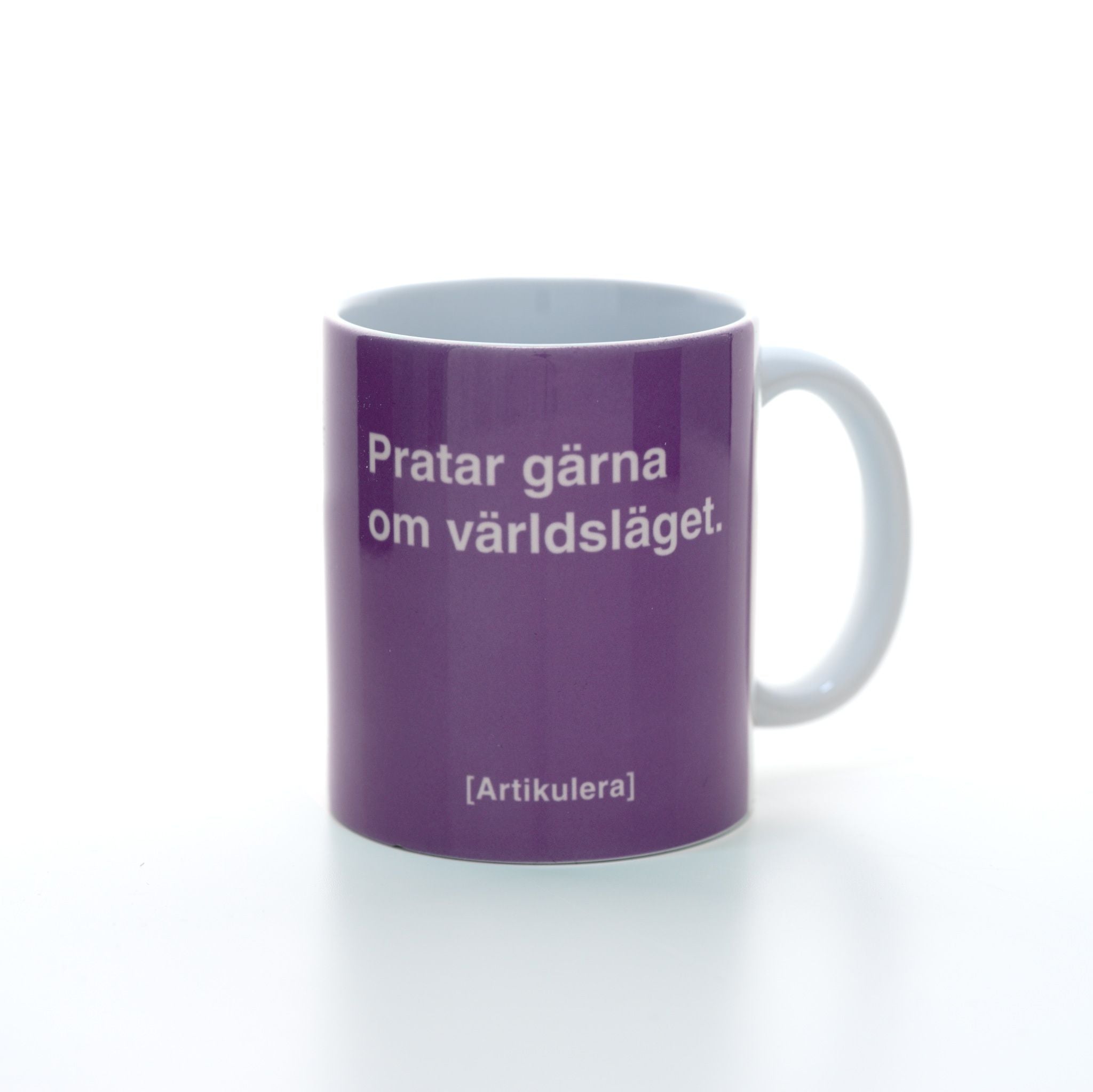Vit mugg med plommonlila tryck, vit text ”Pratar gärna om världsläget.” samt vit Artikulera-logotyp