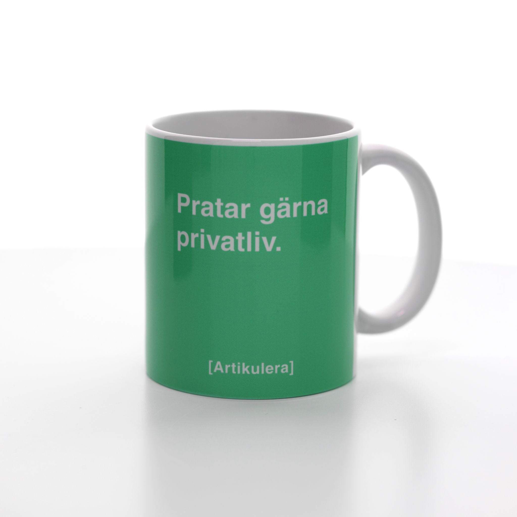 Vit mugg med klargrönt tryck, vit text ”Pratar gärna privatliv.” samt vit Artikulera-logotyp