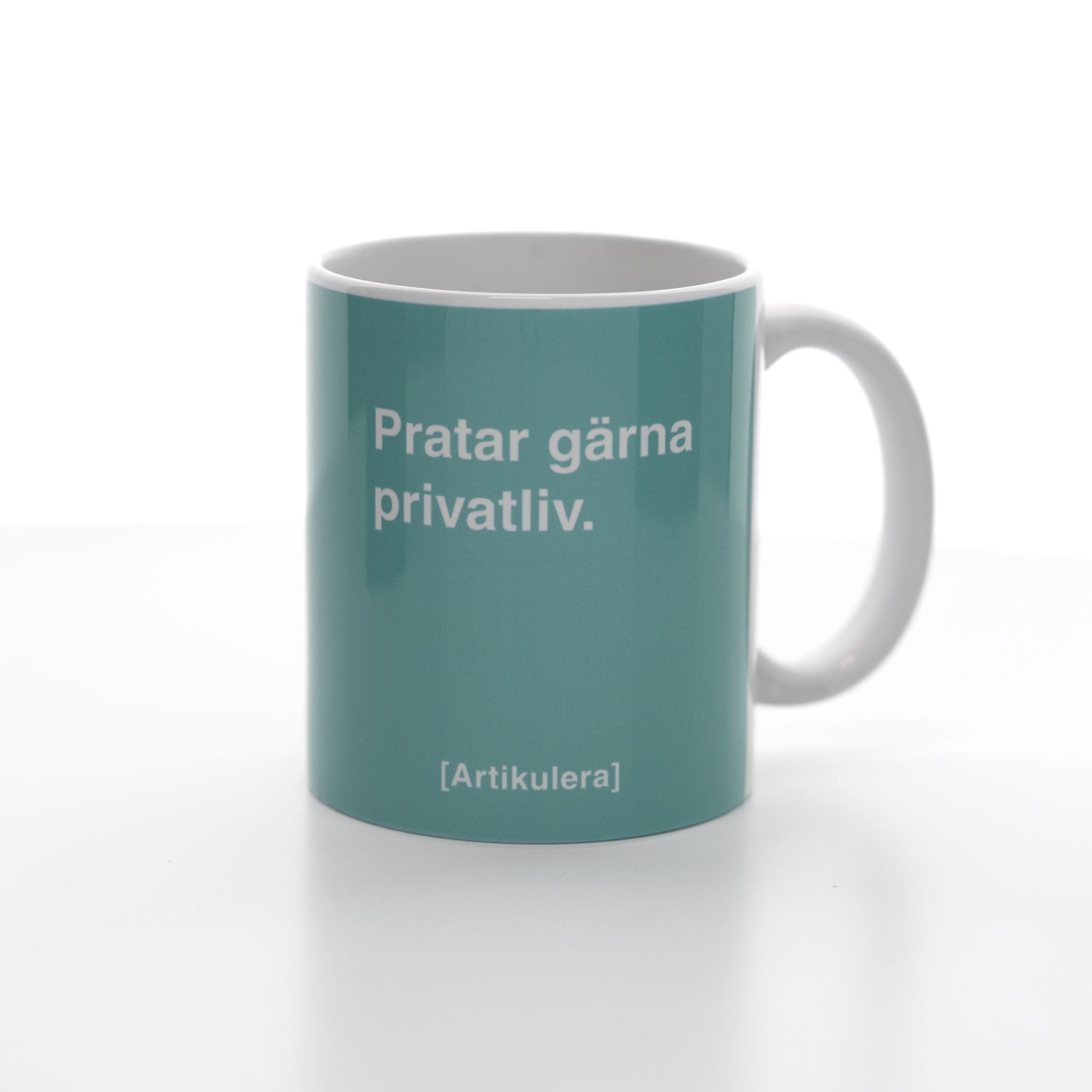 Vit mugg med ljus blågrönt tryck, vit text ”Pratar gärna privatliv.” samt vit Artikulera-logotyp