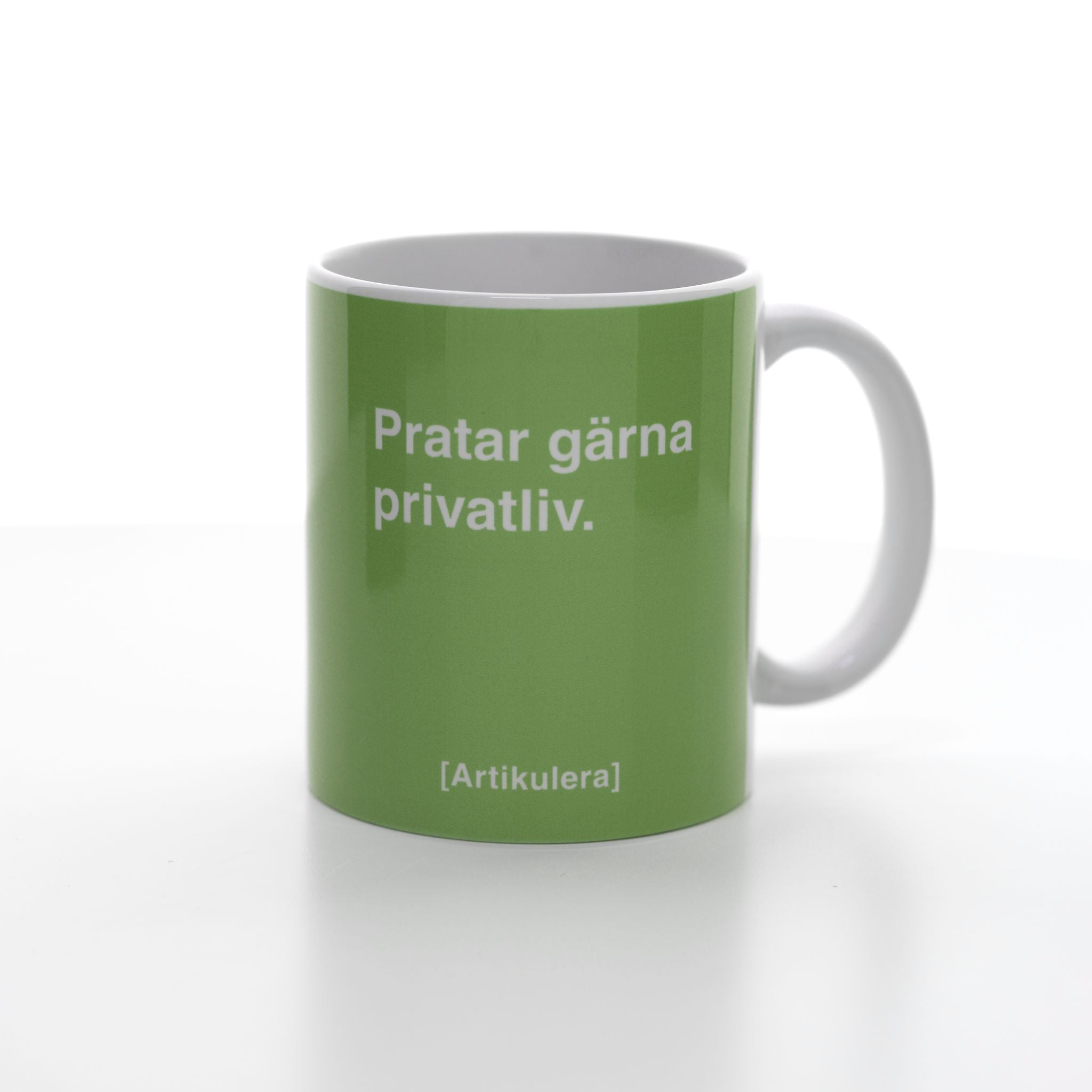 Vit mugg med ljust limegrönt tryck, vit text ”Pratar gärna privatliv.” samt vit Artikulera-logotyp
