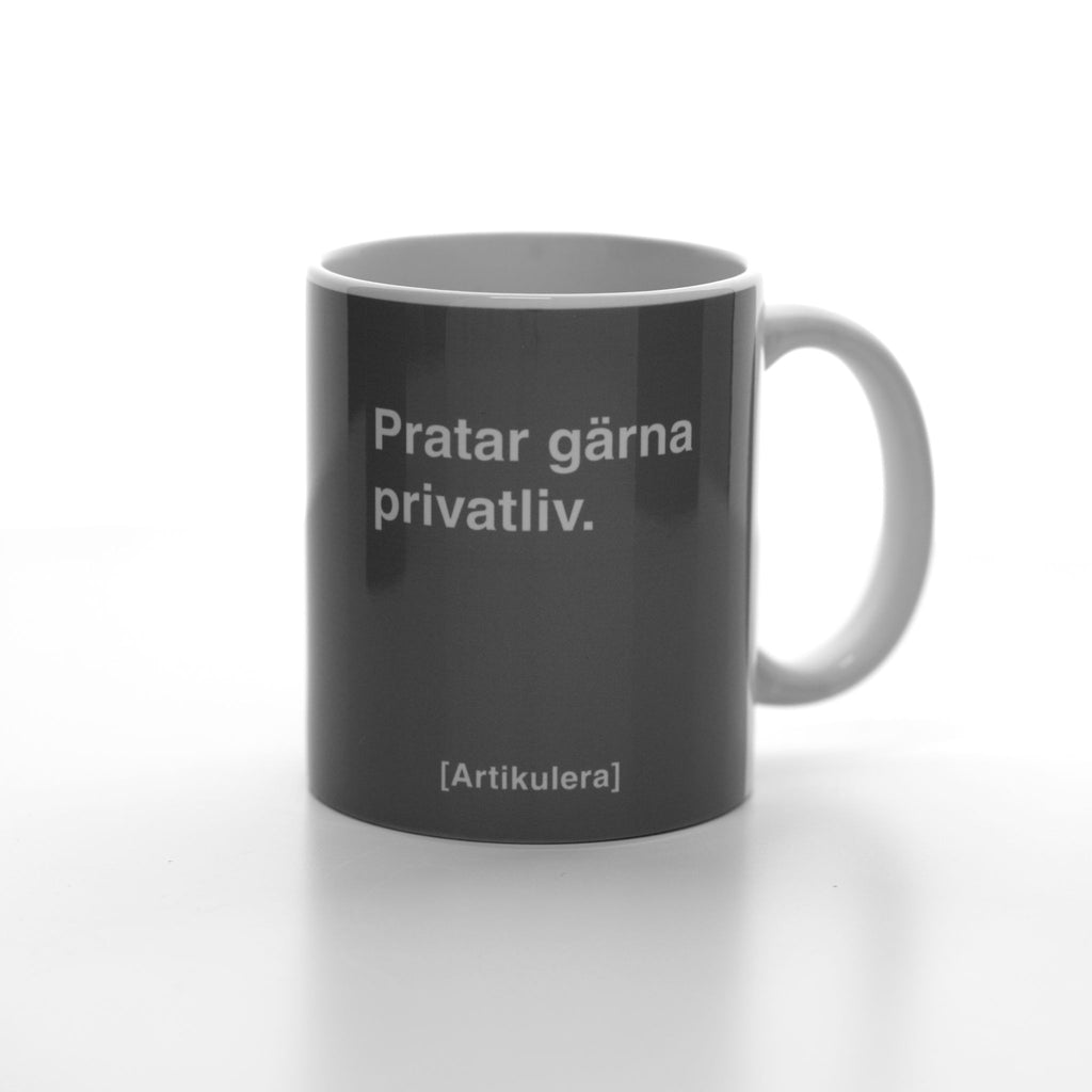 Vit mugg med mörkt rockigt grått tryck, vit text ”Pratar gärna privatliv.” samt vit Artikulera-logotyp