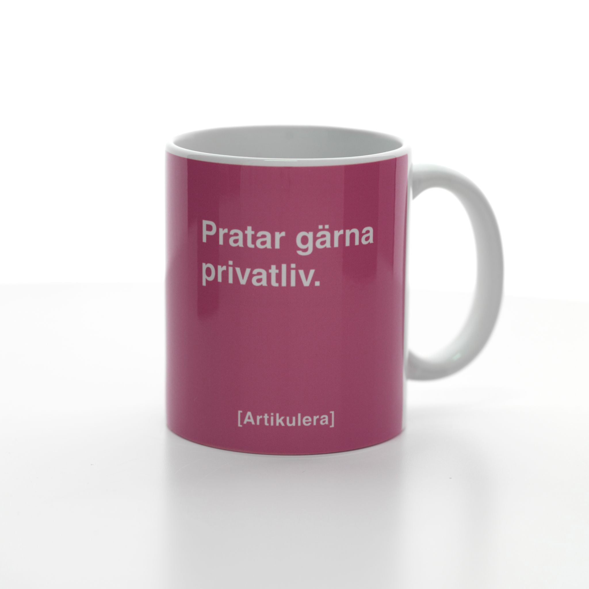 Vit mugg med rosa tryck, vit text ”Pratar gärna privatliv.” samt vit Artikulera-logotyp